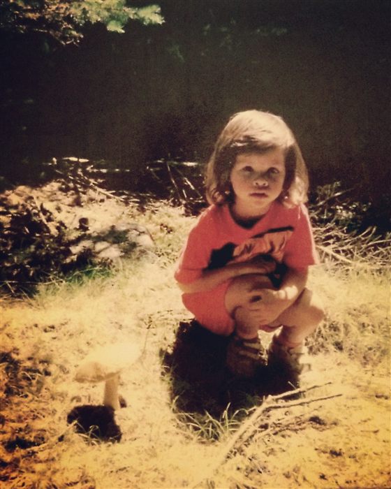 A young Robin crouched in the woods beside a small mushroom